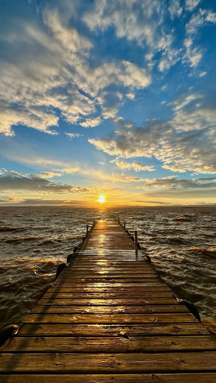 A wooden pier stretching into the Albufera lagoon at sunset, clouds lit gold