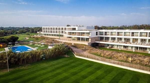 A modern white hotel above a green lawn near the coast