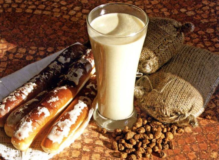 A tall glass of horchata beside fartons and tiger nuts