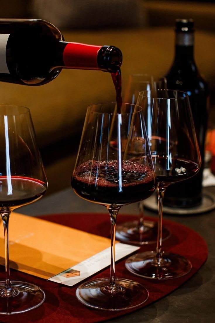 Red wine being poured into glasses on a wooden table in a dimly lit room